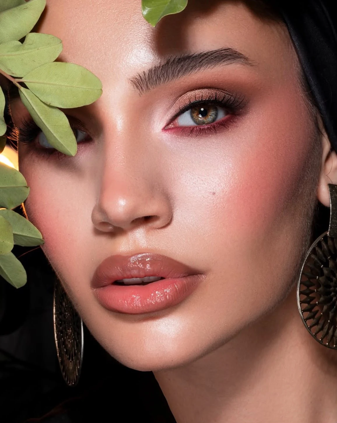 Soft rose-gold eyes, glowing skin and glossy lips framed by leaves.